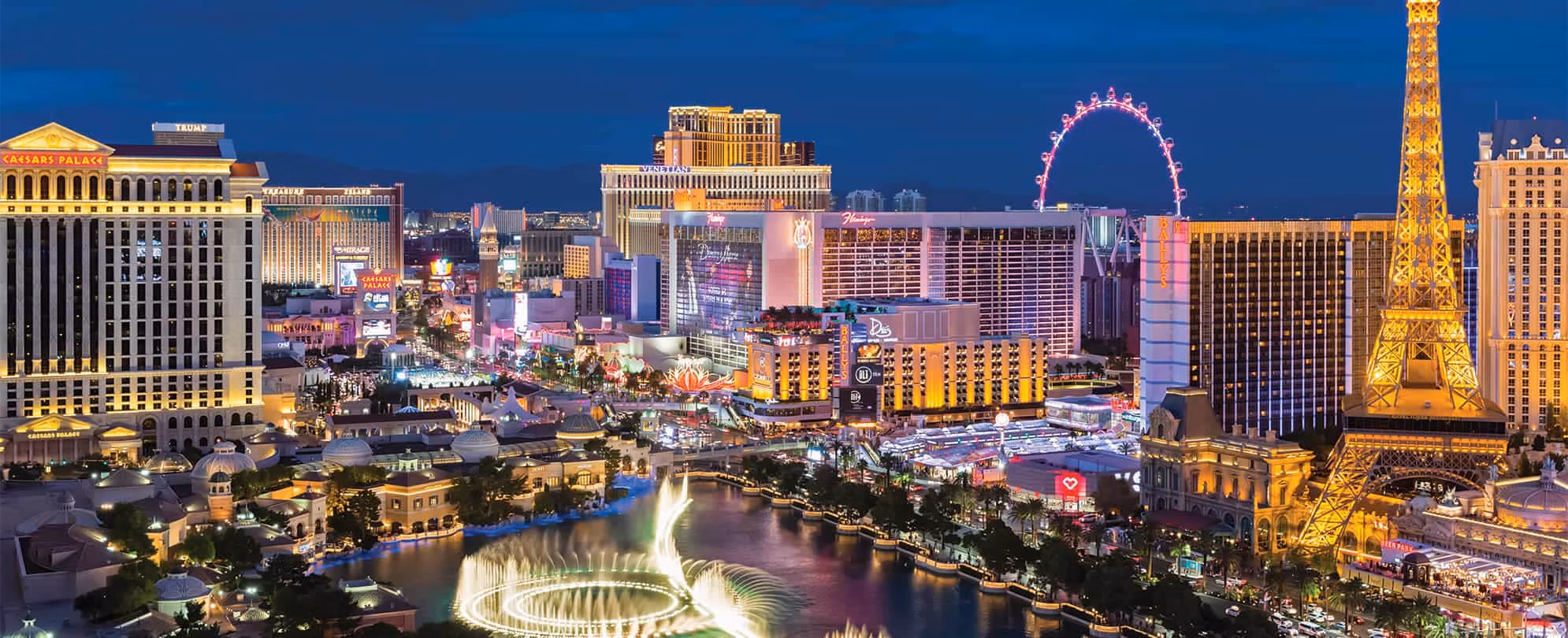 The Las Vegas Strip at dusk, with the Bellagio fountains, Caesars Palace, and the High Roller observation wheel lit up.