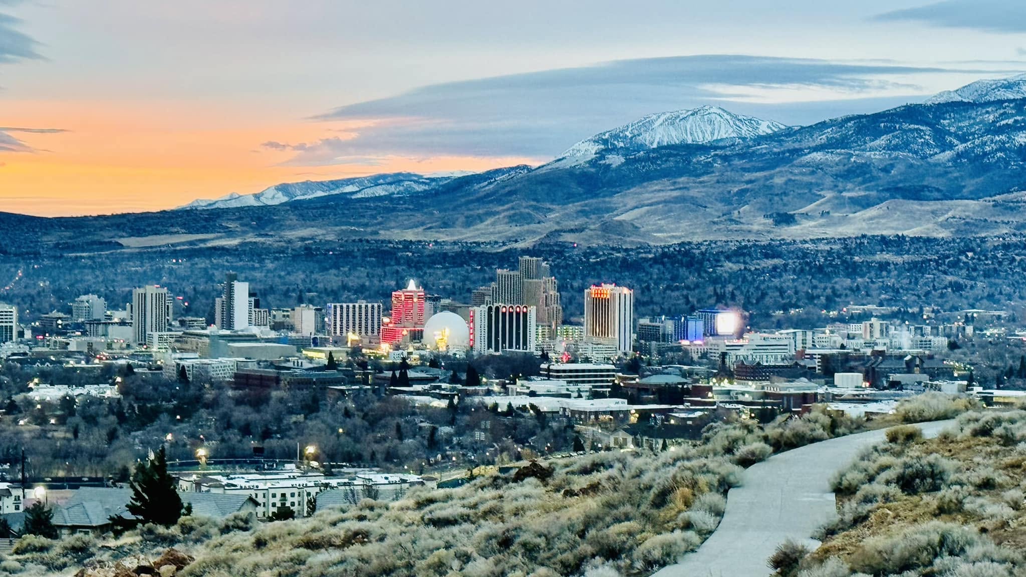 Downtown Reno at sunset, with snow-covered mountains rising behind the Truckee Meadows.